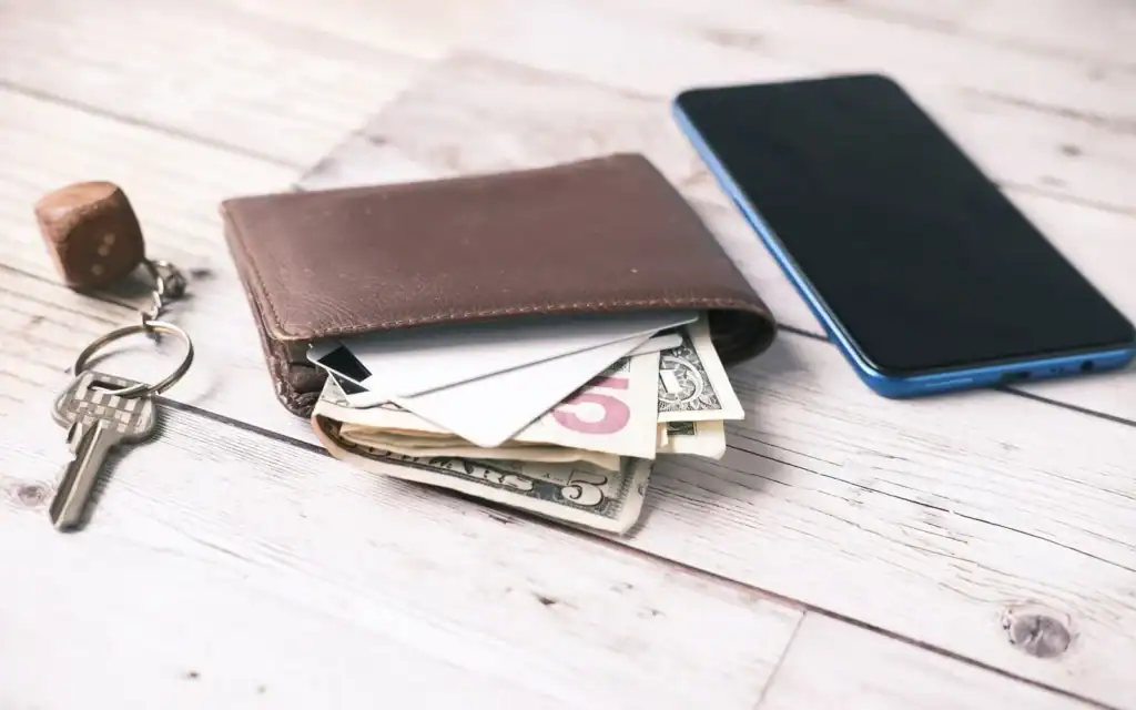 Lommebok med sedler, nøkler og mobiltelefon på et bord