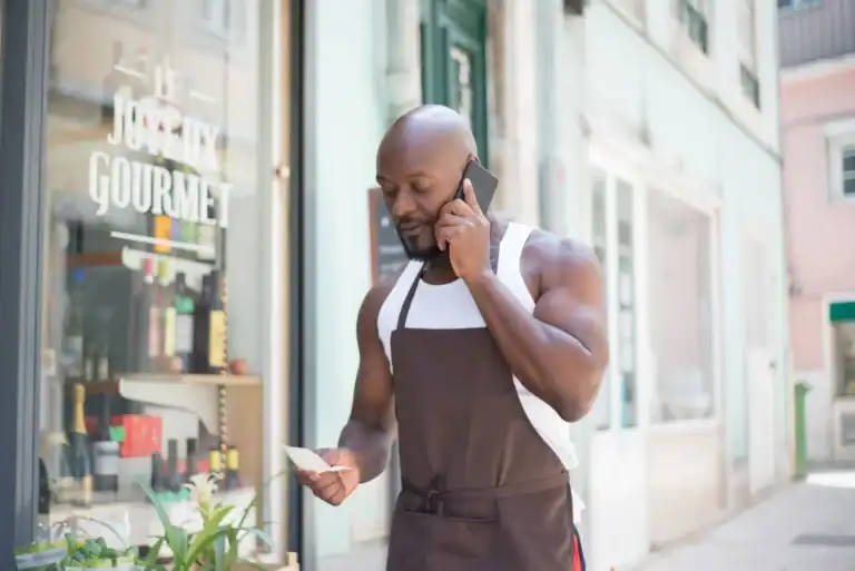 Butikkeier i forkle tar en telefon utenfor butikken