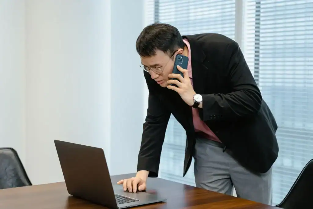 Bedriftsleder sammenligner mobilabonnement på telefon og PC på kontoret