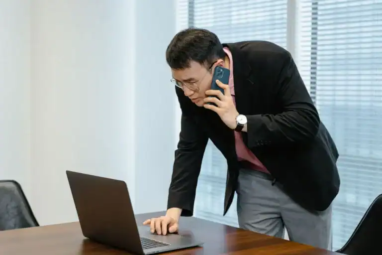 Bedriftsleder sammenligner mobilabonnement på telefon og PC på kontoret