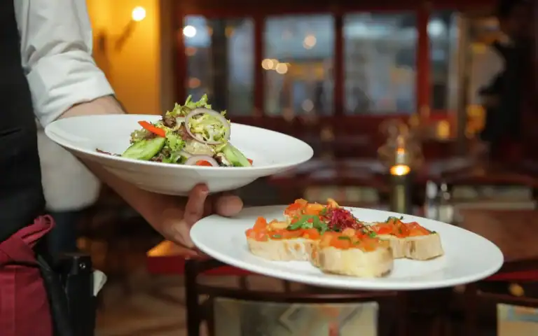 Servitør bærer tallerkener gjennom restaurantlokalet