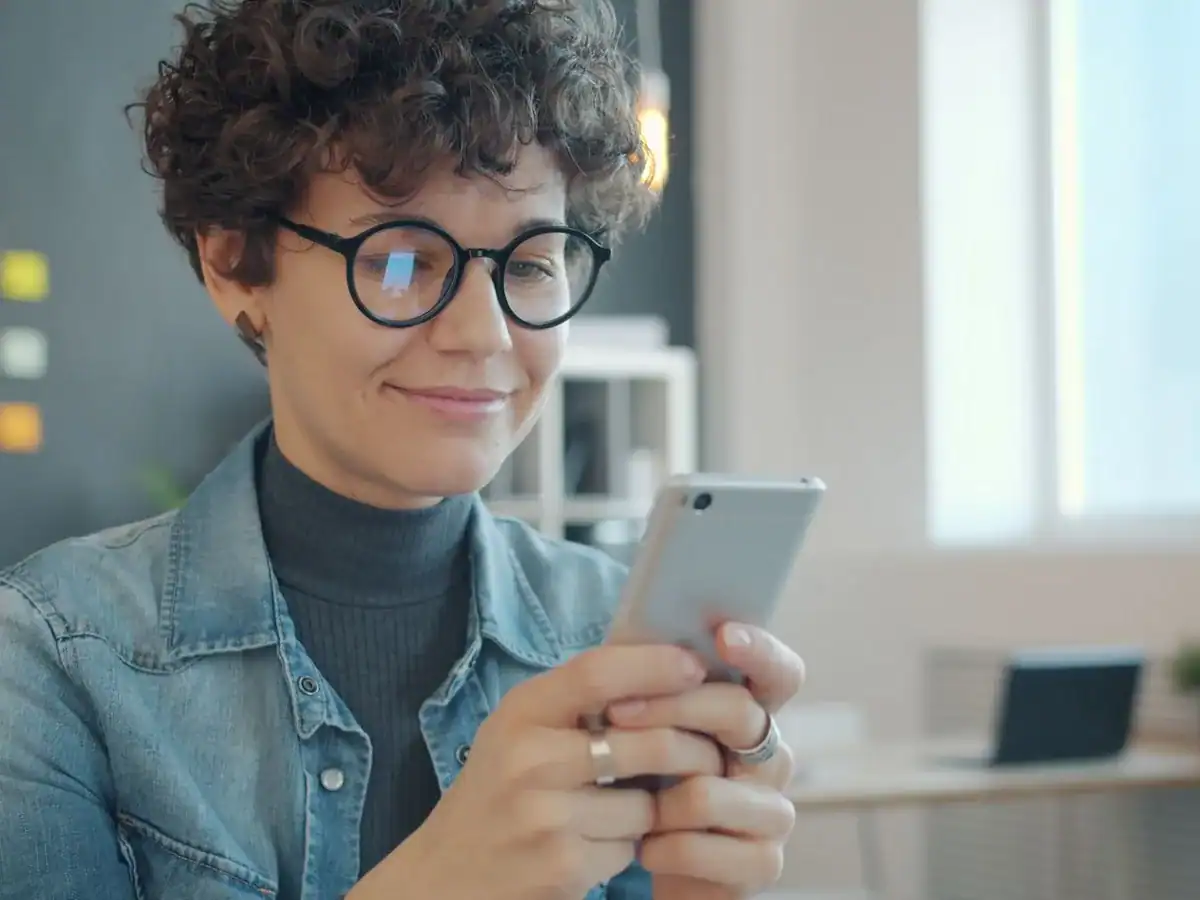 Ansatt leser på mobilen ved skrivebordet i et lyst kontor