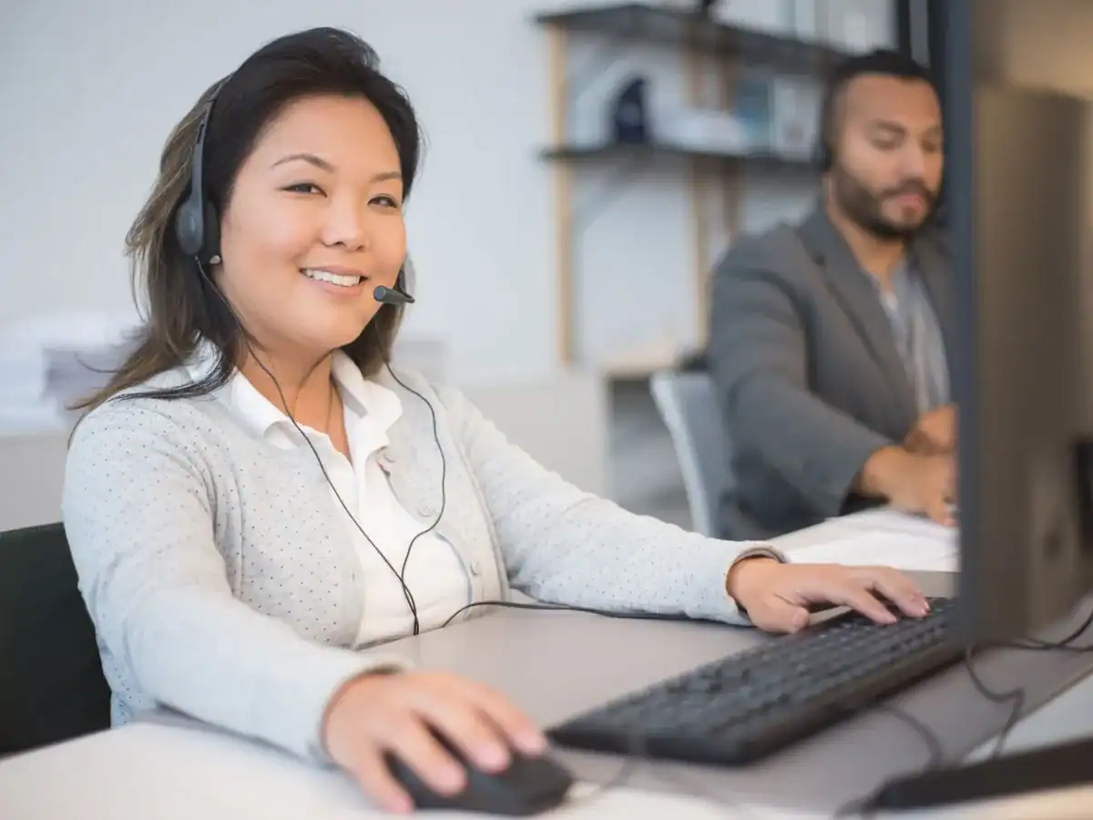 To kundeservicemedarbeidere med headset ved skjermene sine