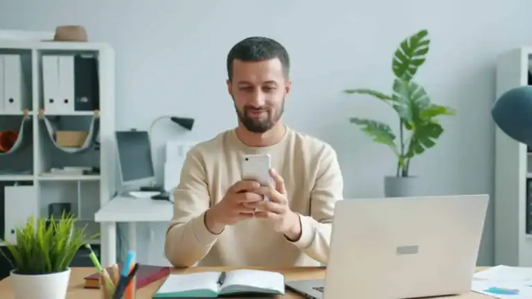 Mann smiler mens han ser pa smarttelefonen sin pa et moderne kontor